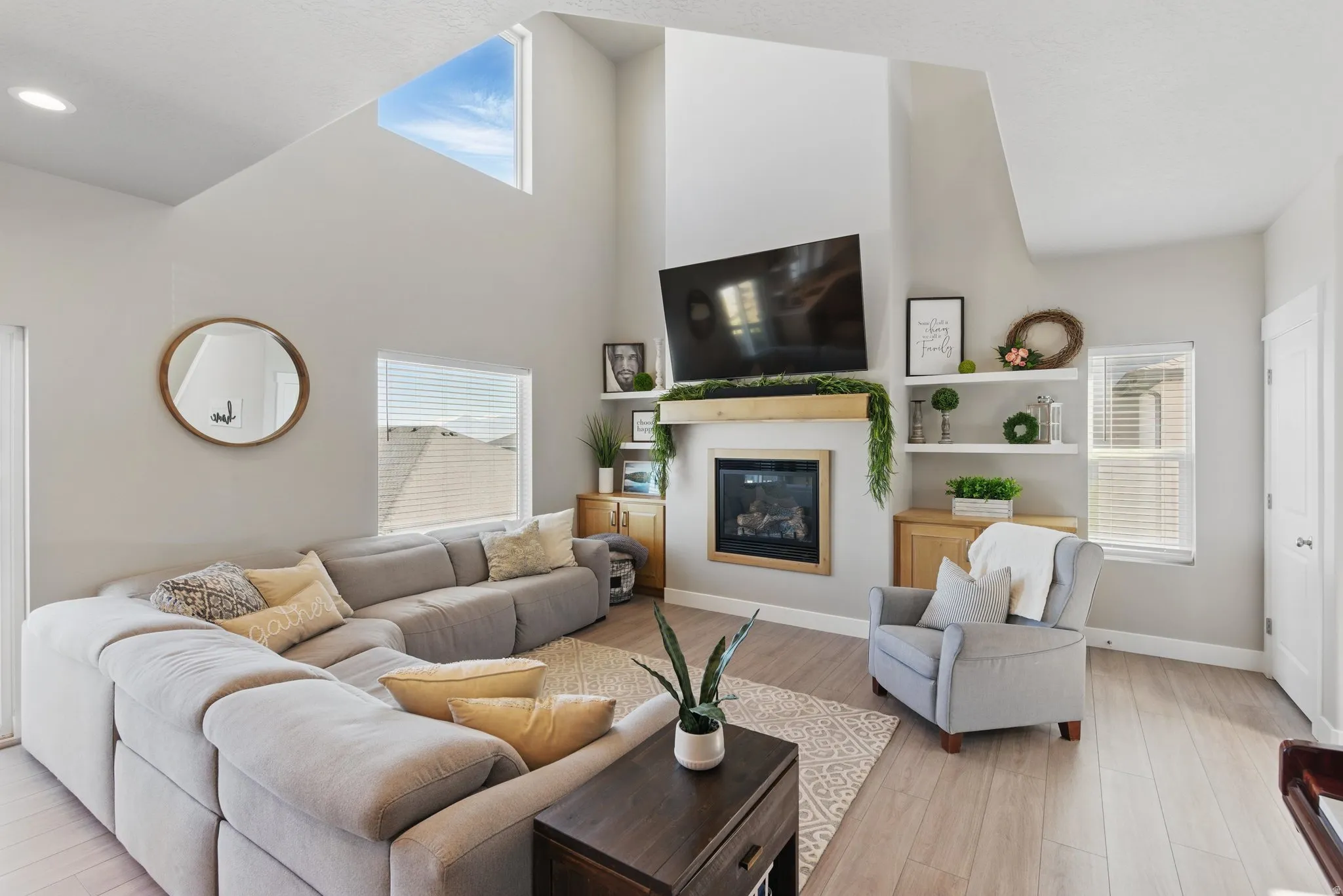 Living room with a high ceiling, light wood finished floors, and a glass covered fireplace