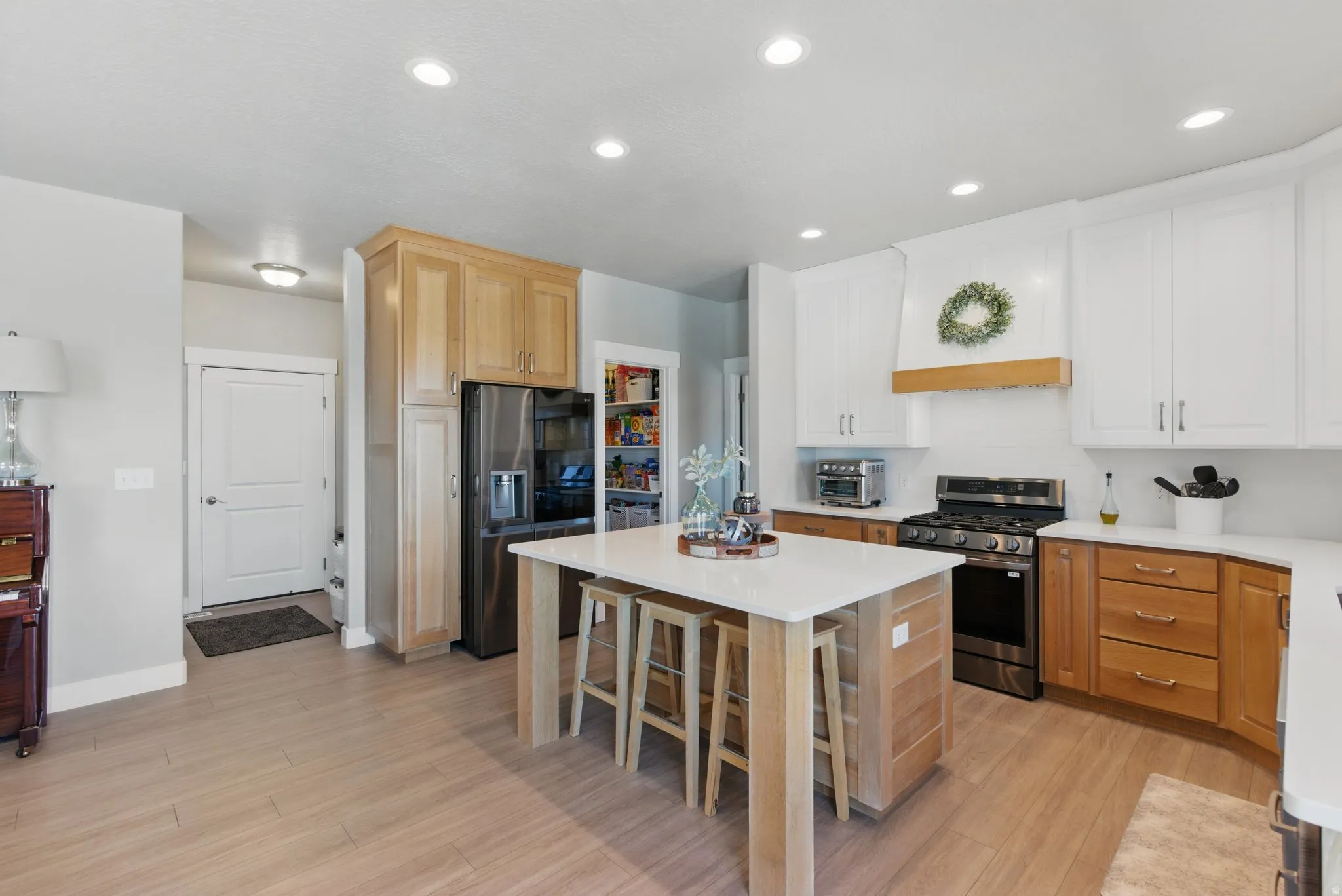 Two tone kitchen featuring stainless steel appliances, recessed lighting, light wood finished floors, a kitchen island, and a breakfast bar