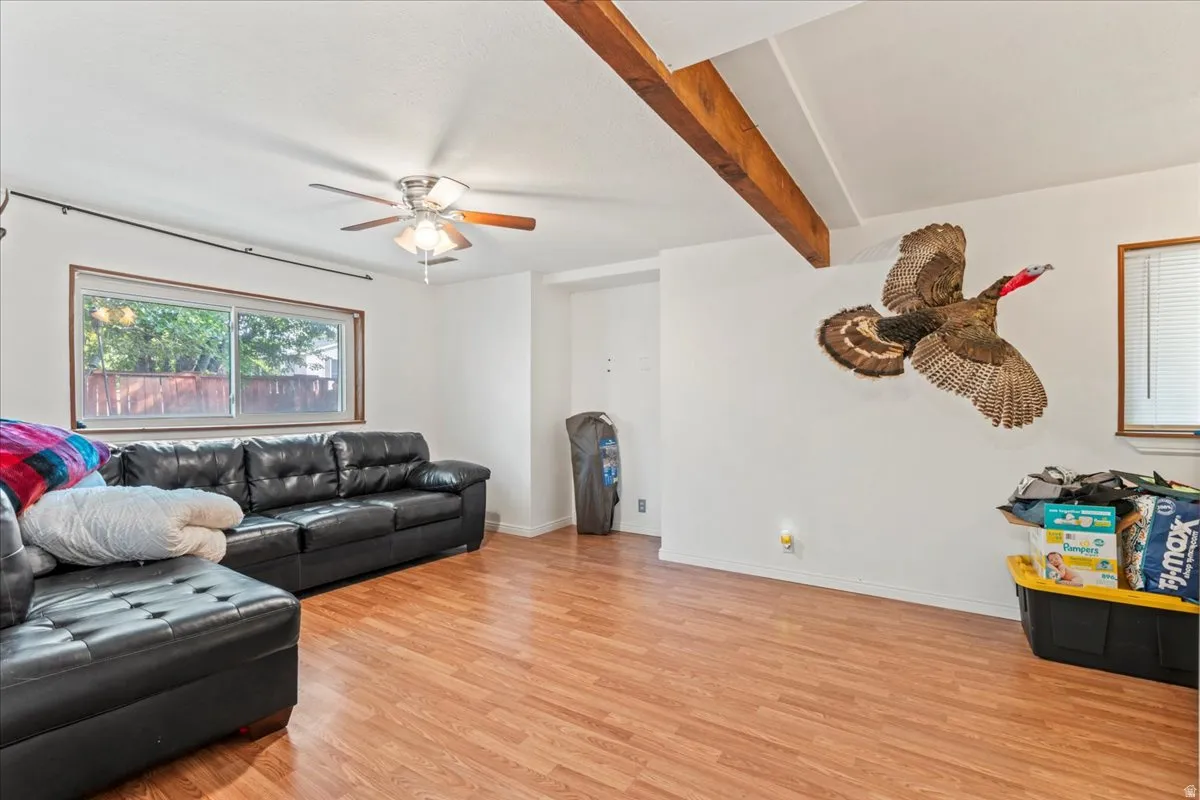 Living room featuring light wood-style flooring, beam ceiling, and a ceiling fan