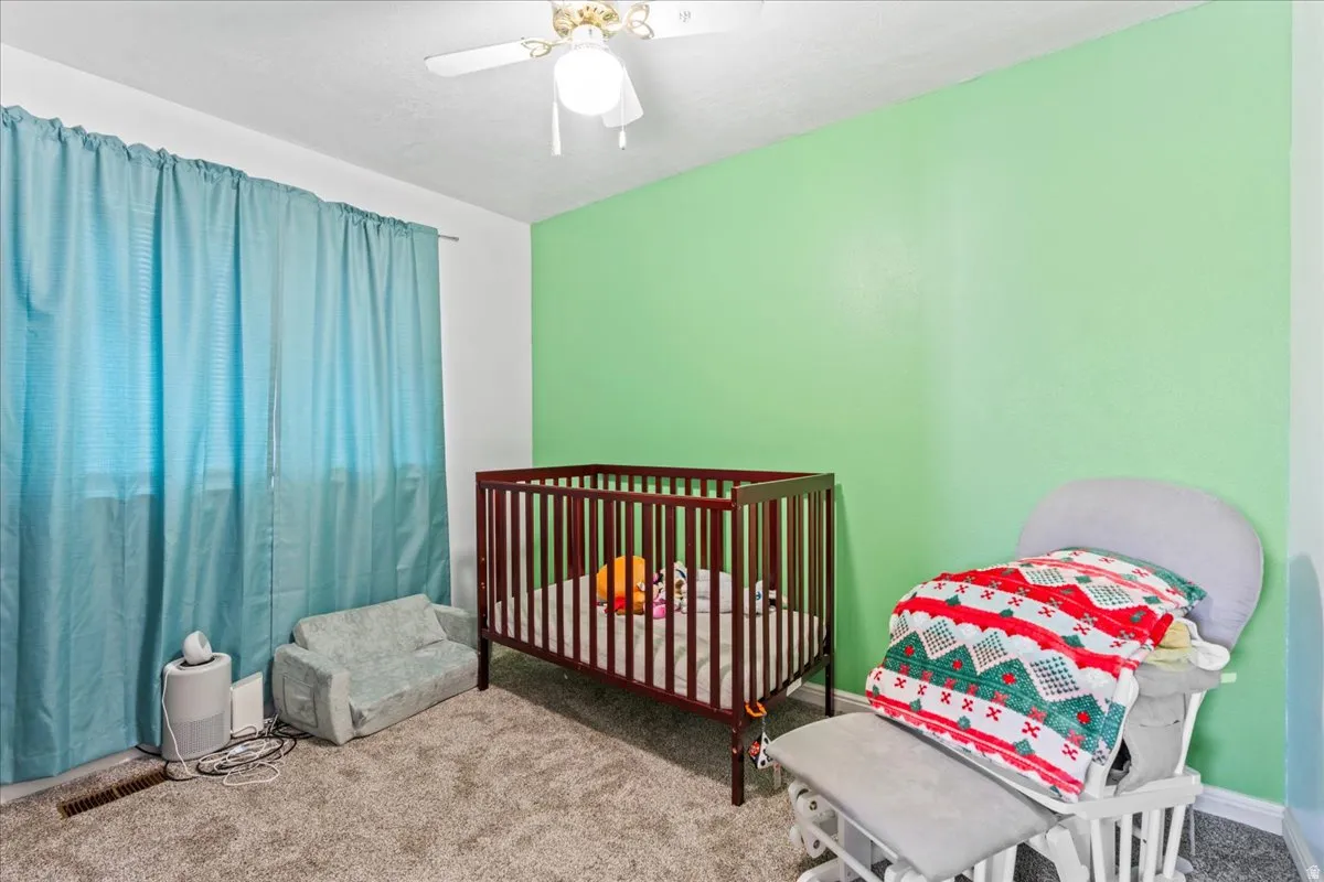 Bedroom with carpet flooring, a nursery area, and a ceiling fan