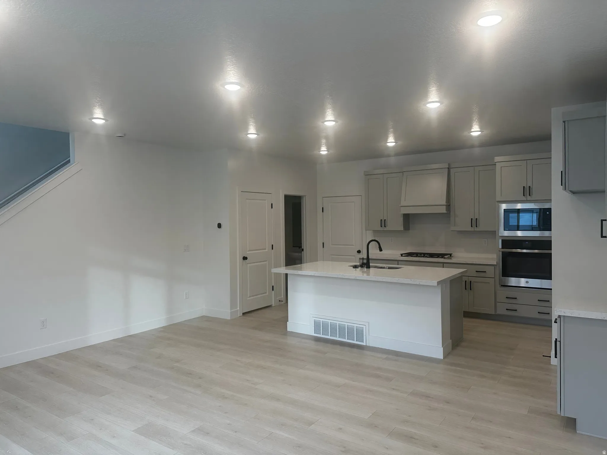 Kitchen with stainless steel appliances, gray cabinetry, an island with sink, and light wood-type flooring