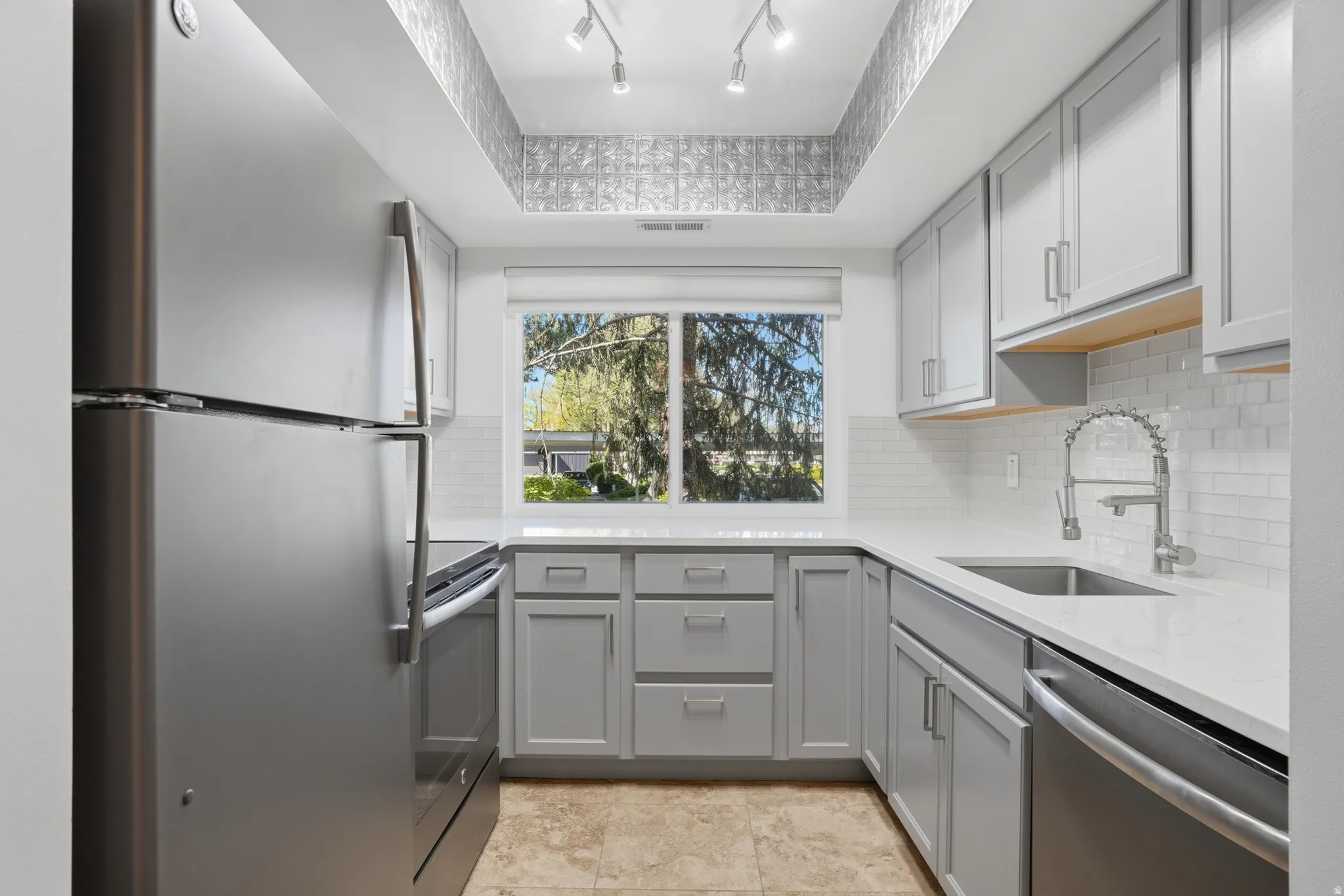 Kitchen with stainless steel appliances, gray cabinetry, a tray ceiling, light quartz counters, and backsplash