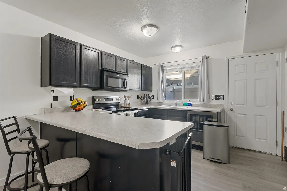Kitchen featuring a breakfast bar area, a peninsula, light countertops, electric stove, and black microwave