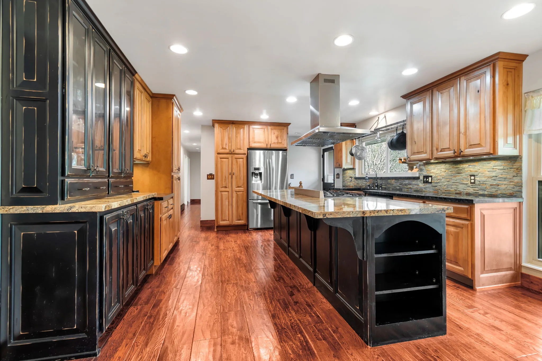 Kitchen with dark stone countertops, two tone cabinetry, a breakfast bar area, stainless steel refrigerator with ice dispenser, and dark wood-type flooring