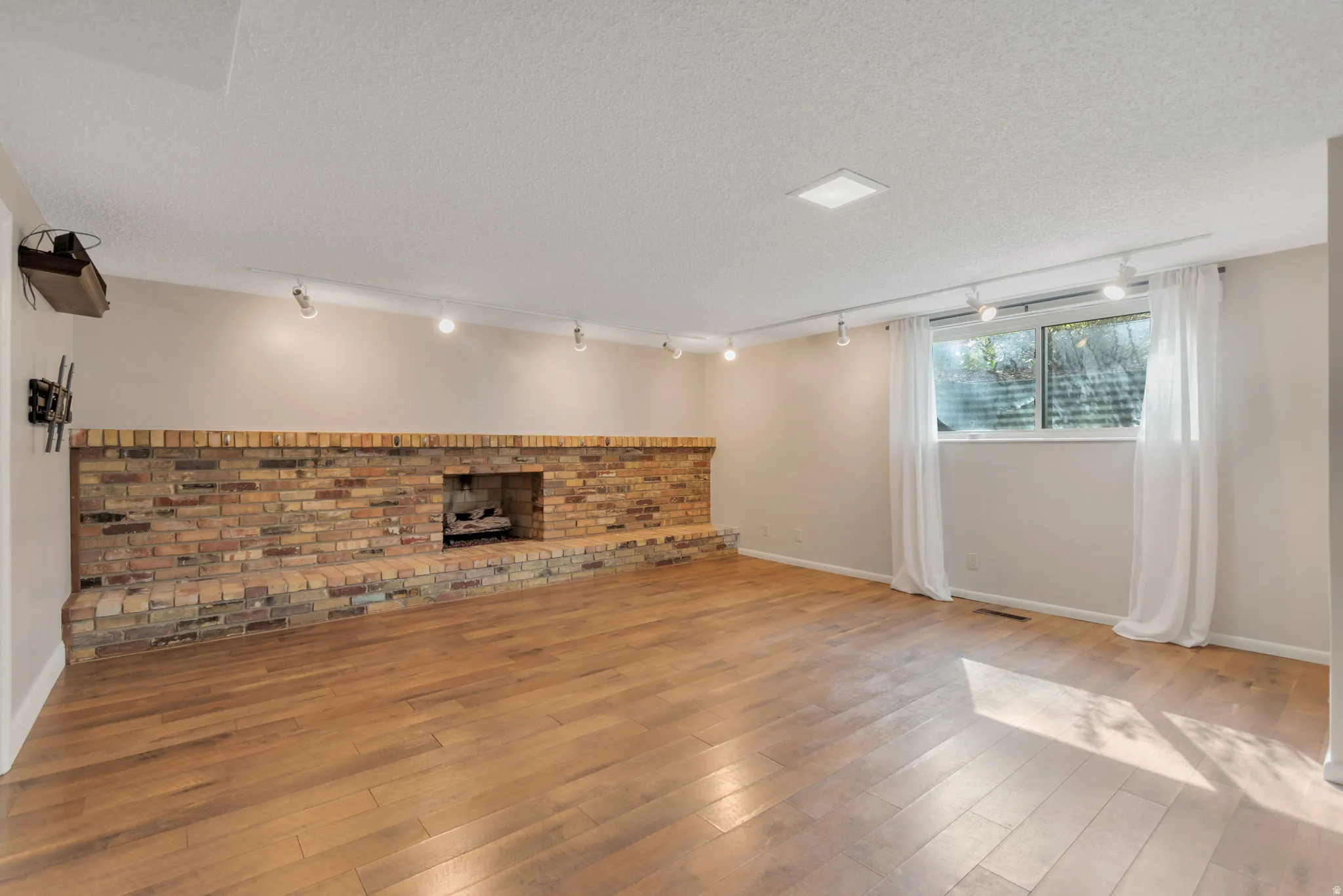 Unfurnished living room with track lighting, a textured ceiling, hardwood / wood-style floors, and a brick fireplace