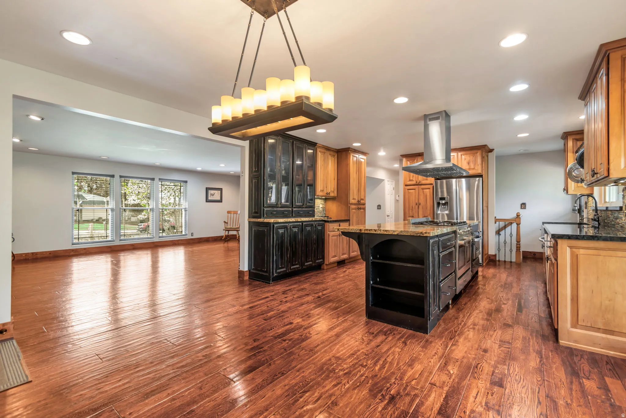 Two tone kitchen with dark stone counters, open shelves, a center island, island range hood, and tasteful backsplash
