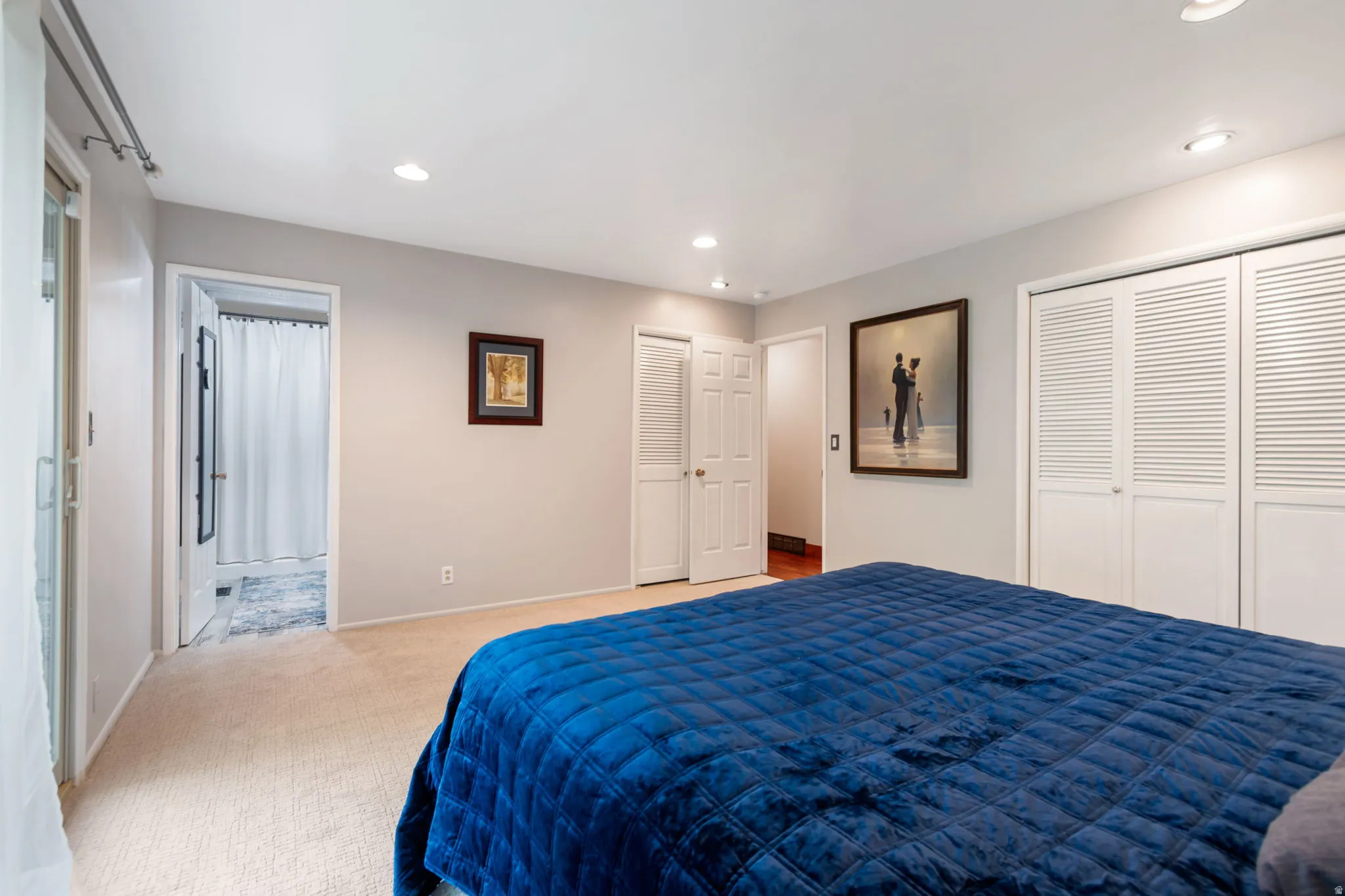 Bedroom with ensuite bath, light carpet, recessed lighting, and multiple closets