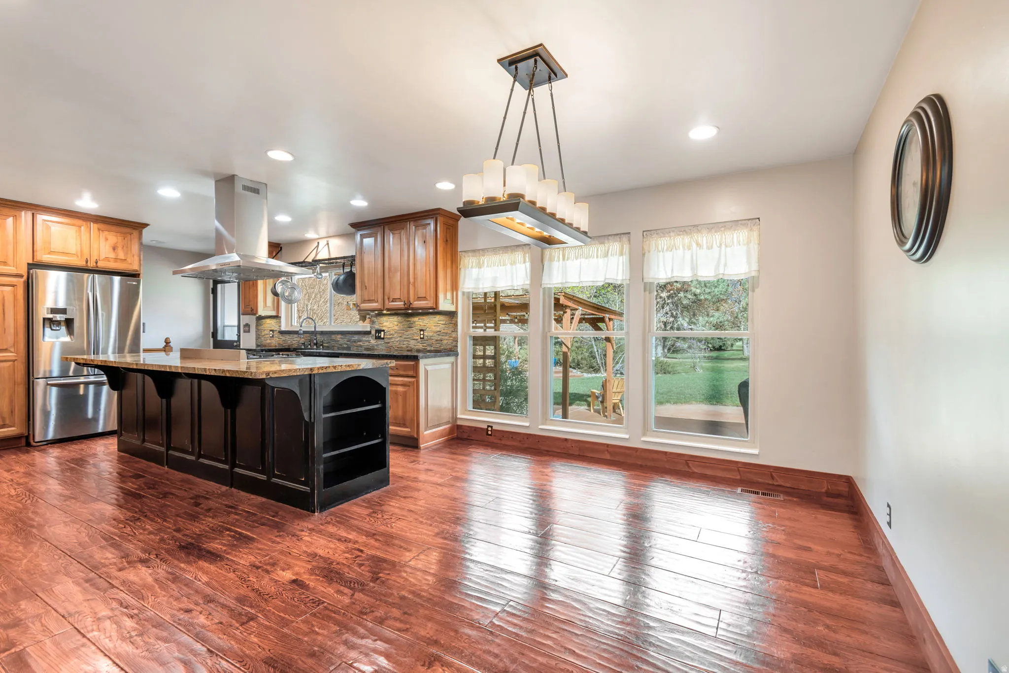 Kitchen with stainless steel fridge with ice dispenser, a breakfast bar area, island range hood, dark stone countertops, and dark wood-type flooring
