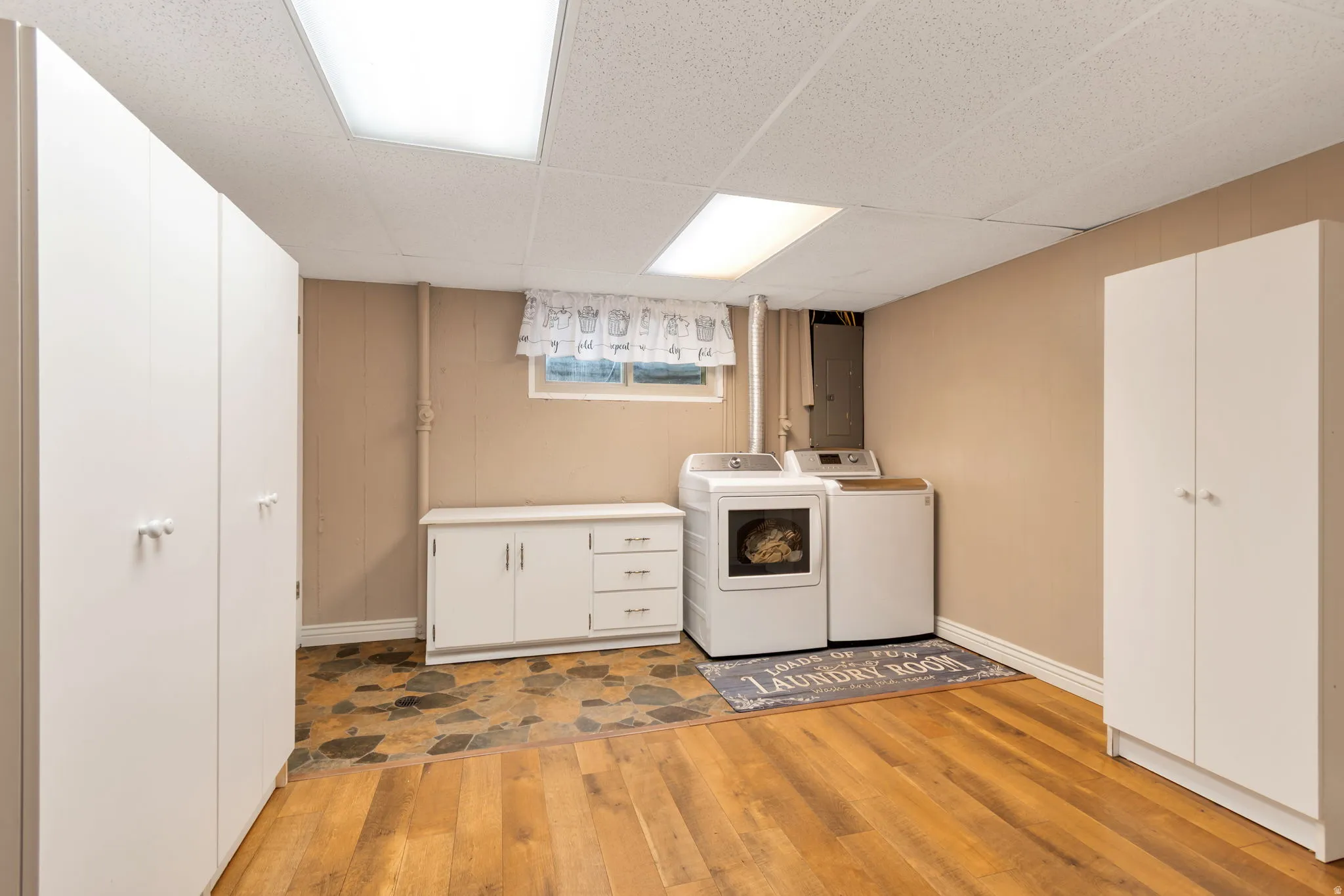 Laundry room featuring cabinet space, light wood-style floors, a paneled ceiling, washing machine and clothes dryer, and electric panel