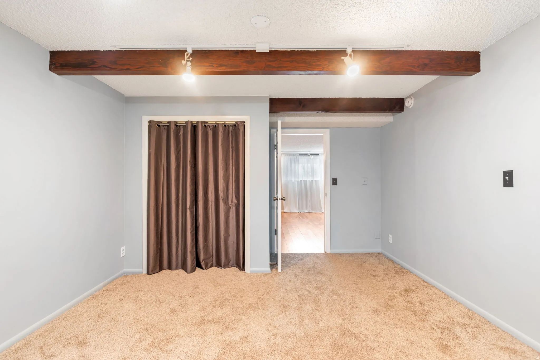 Spare room with a textured ceiling, beamed ceiling, carpet, and track lighting