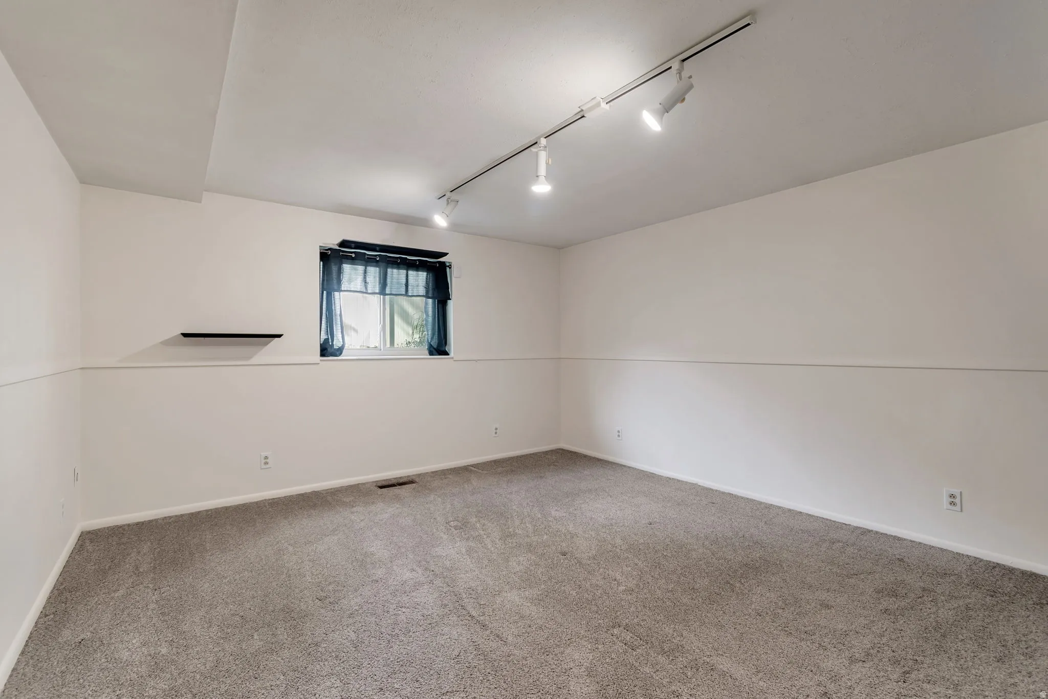Carpeted empty room featuring rail lighting and baseboards