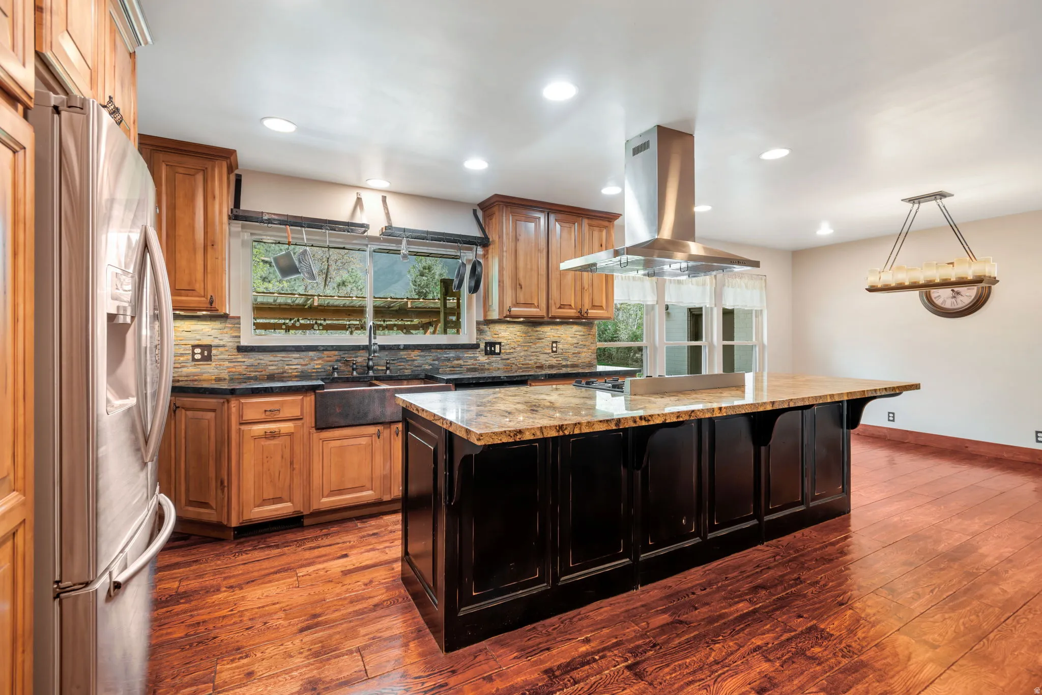 Dual tone kitchen featuring stainless steel refrigerator with ice dispenser, dark wood-type flooring, island exhaust hood, decorative backsplash, and a kitchen island