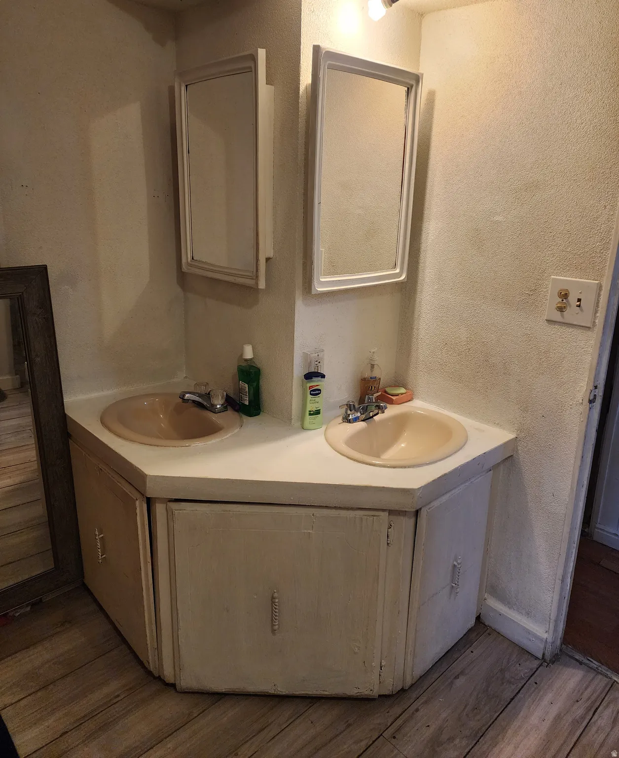 Bathroom featuring double vanity, a textured wall, and dark wood-style flooring