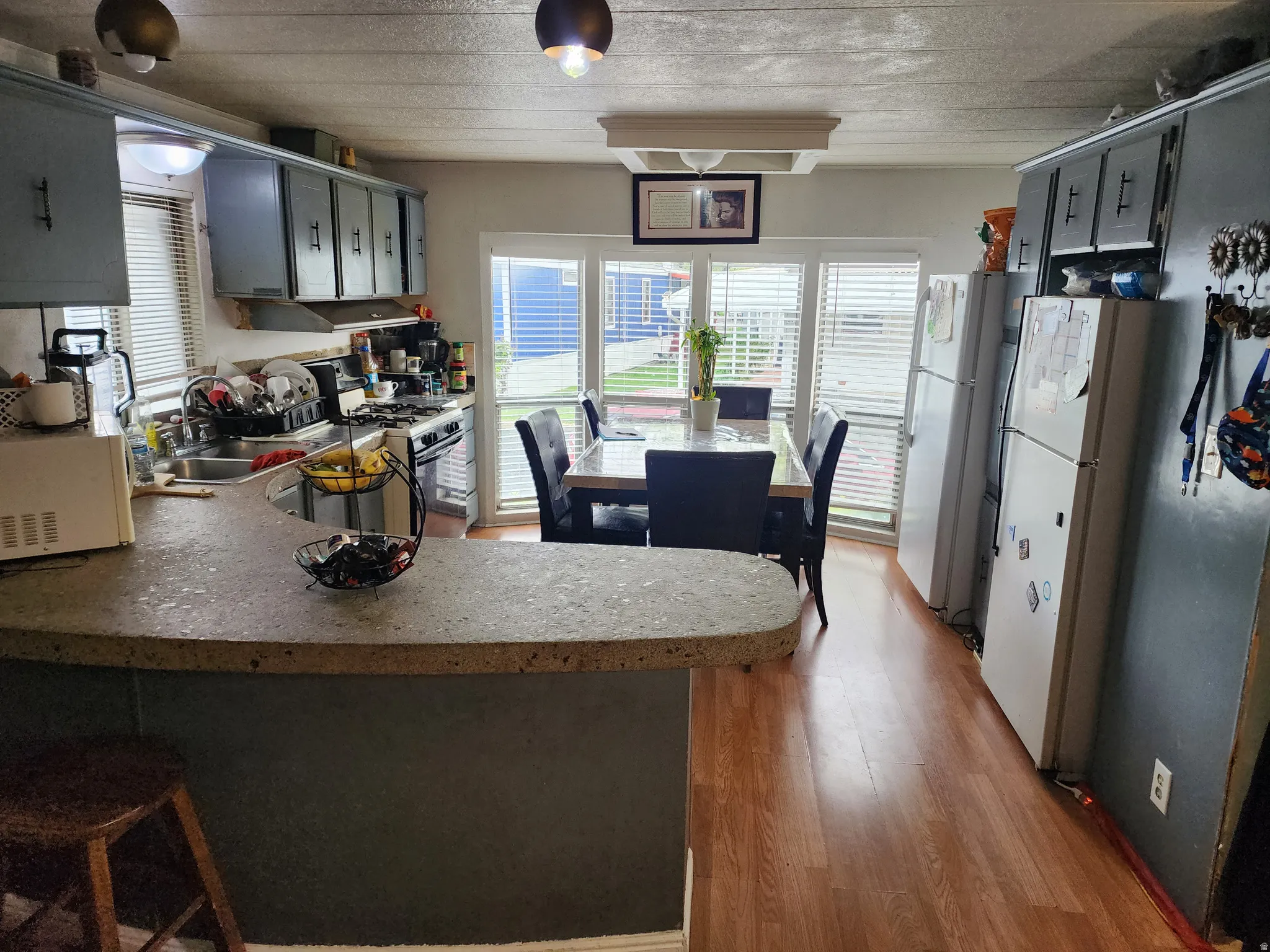 Kitchen with light wood finished floors, a peninsula, white appliances, a breakfast bar area, and gray cabinets