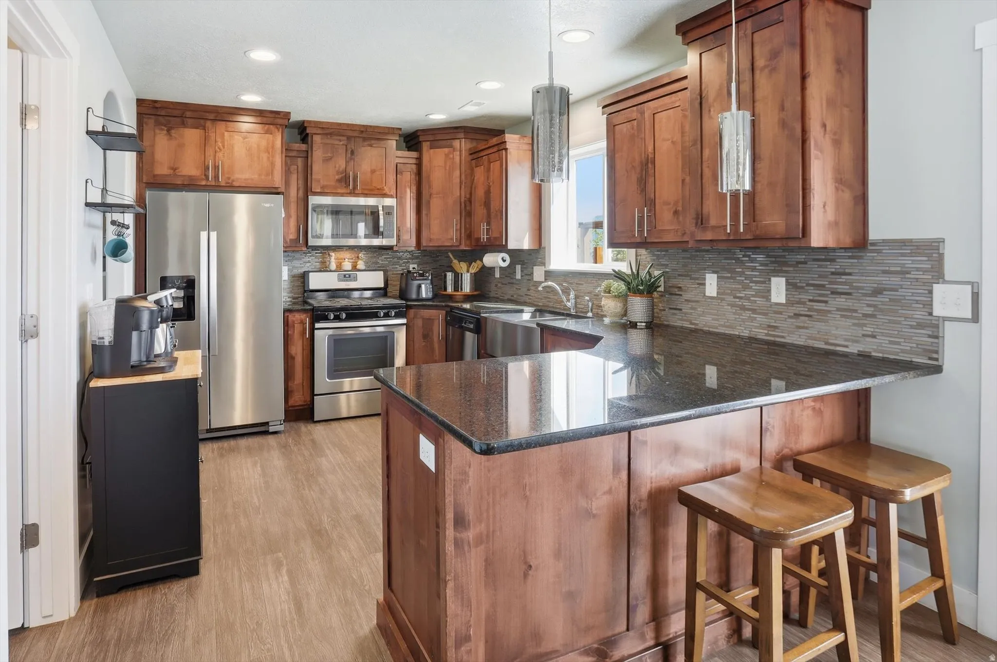 Kitchen featuring stainless steel appliances, a peninsula, wood finish cabinetry, a breakfast bar, and dark stone countertops