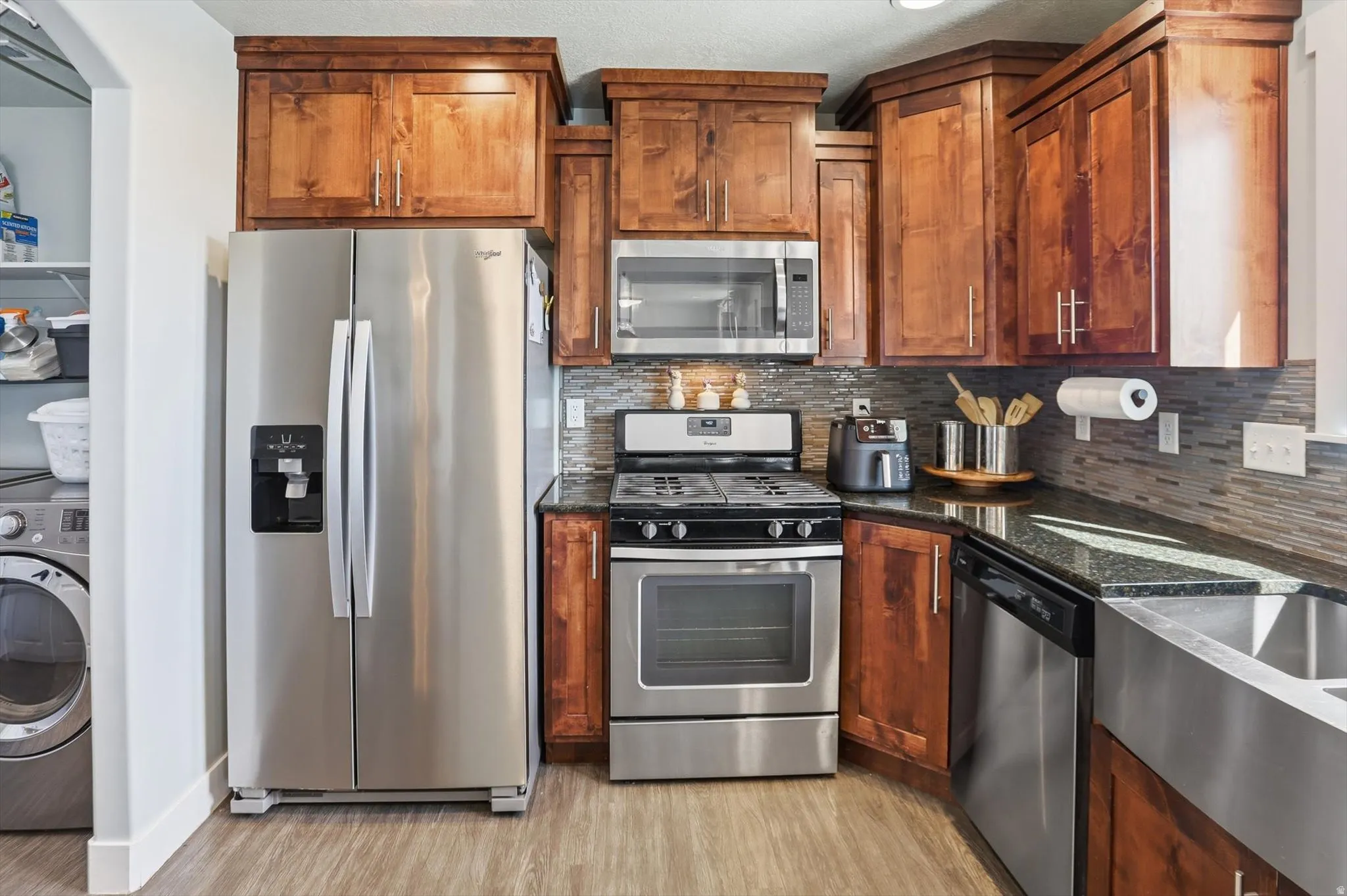 Kitchen with stainless steel appliances, washer / clothes dryer, dark stone countertops, backsplash, and light wood-style floors