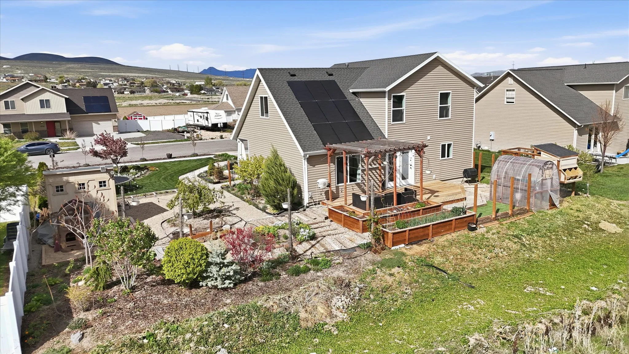 Back of property featuring a deck with mountain view, a vegetable garden, a shingled roof, a pergola, and an outbuilding