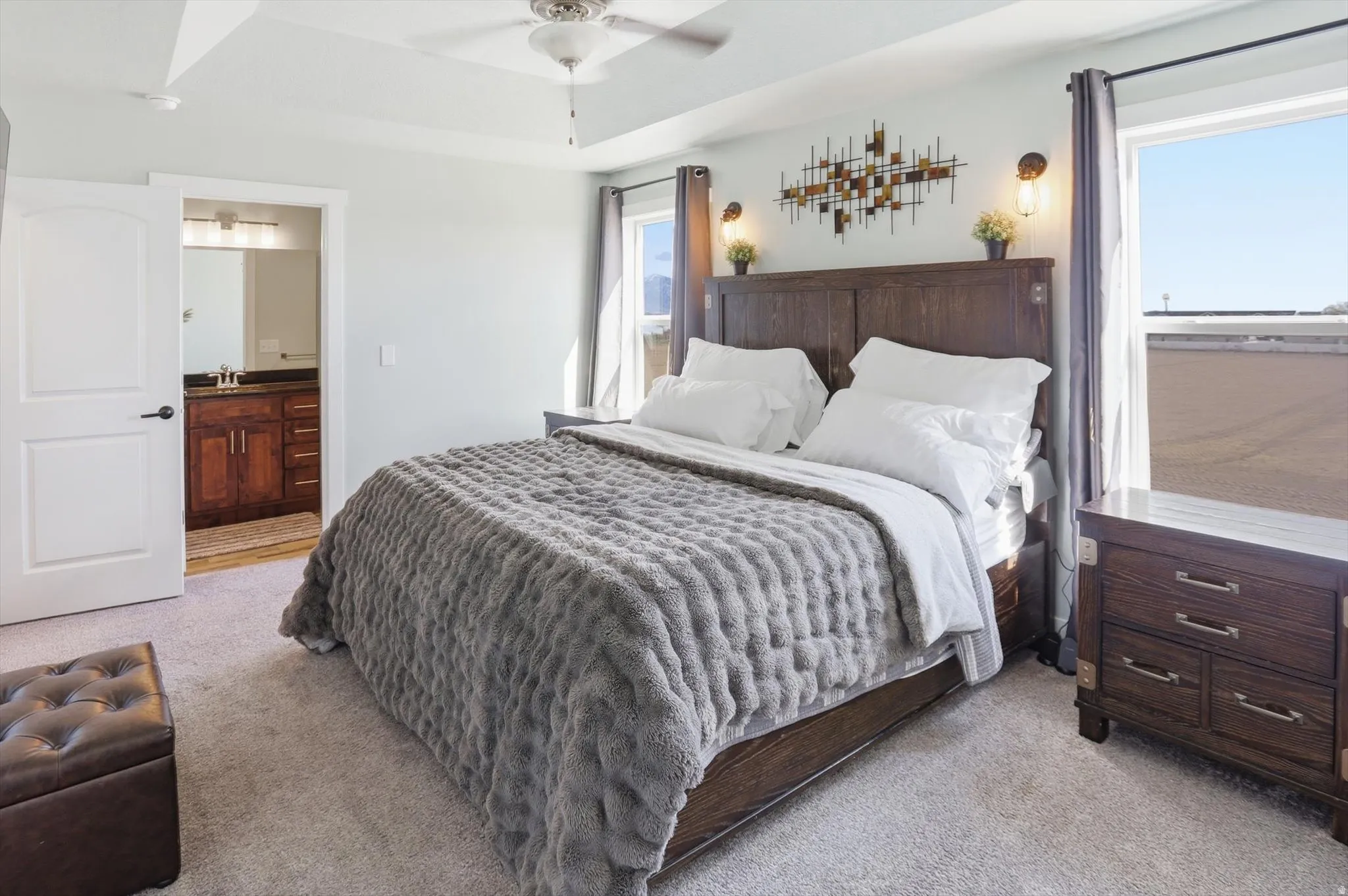 Bedroom featuring light carpet, a raised ceiling, connected bathroom, and ceiling fan