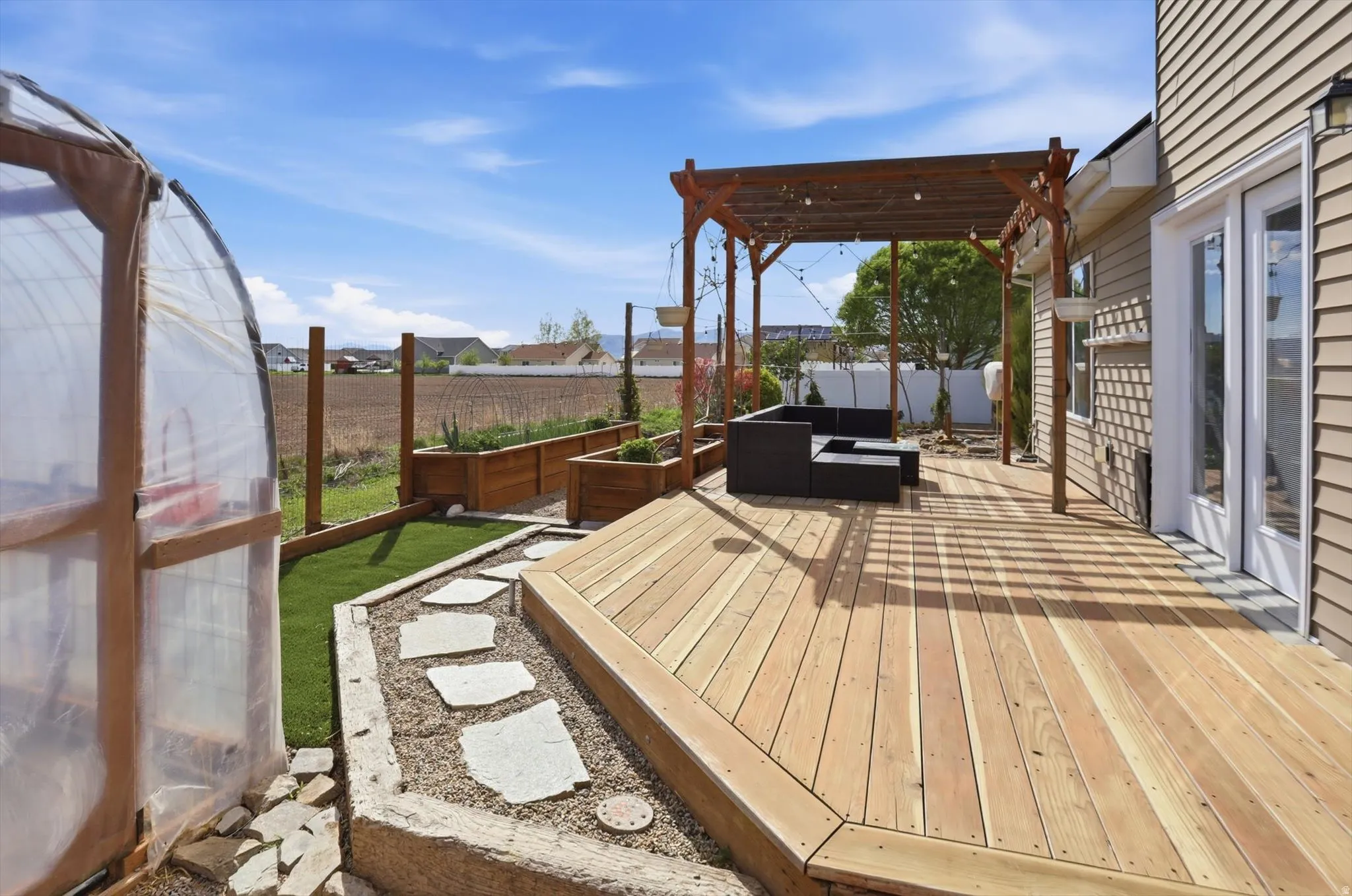 Wooden terrace with a fenced backyard, an outdoor living space, a vegetable garden, an exterior structure, and a pergola