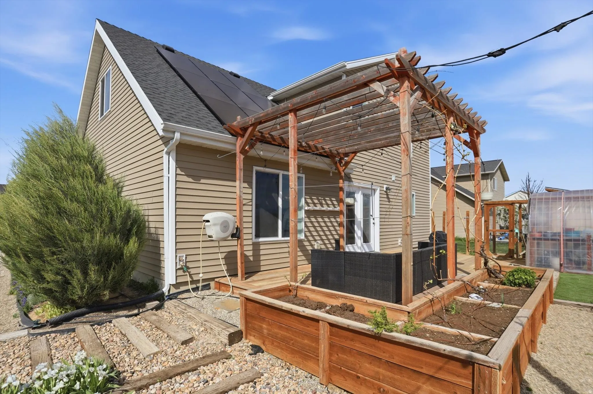 View of front of house featuring a garden, solar panels, roof with shingles, a pergola, and a patio area