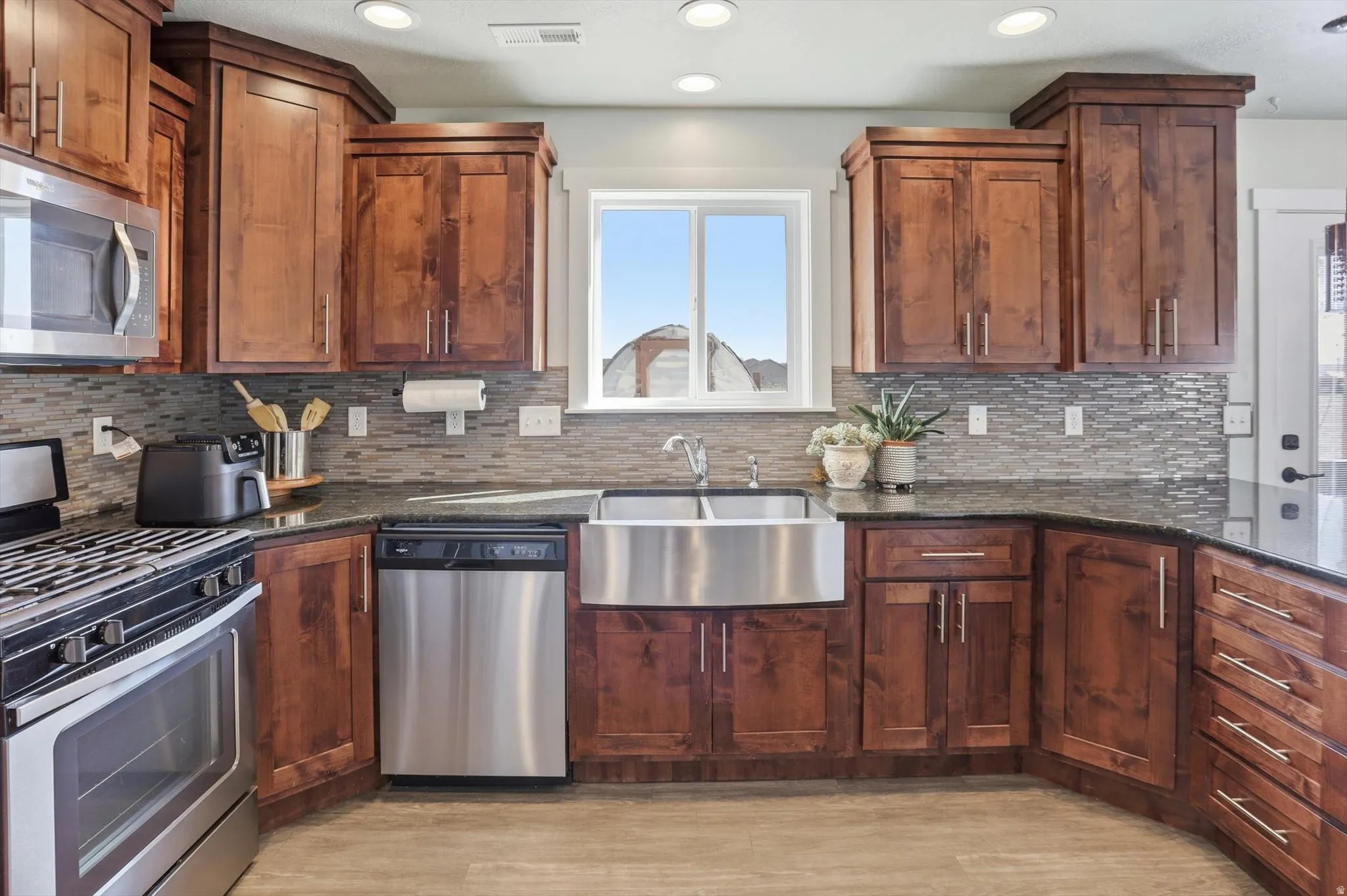Kitchen featuring stainless steel appliances, dark stone countertops, decorative backsplash, recessed lighting, and light wood-style floors