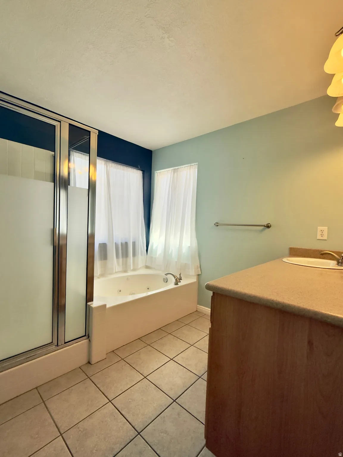 Bathroom featuring a corner jetted tub, separate shower with frosted glass doors, tile flooring, and a wood-finish vanity with an integrated sink