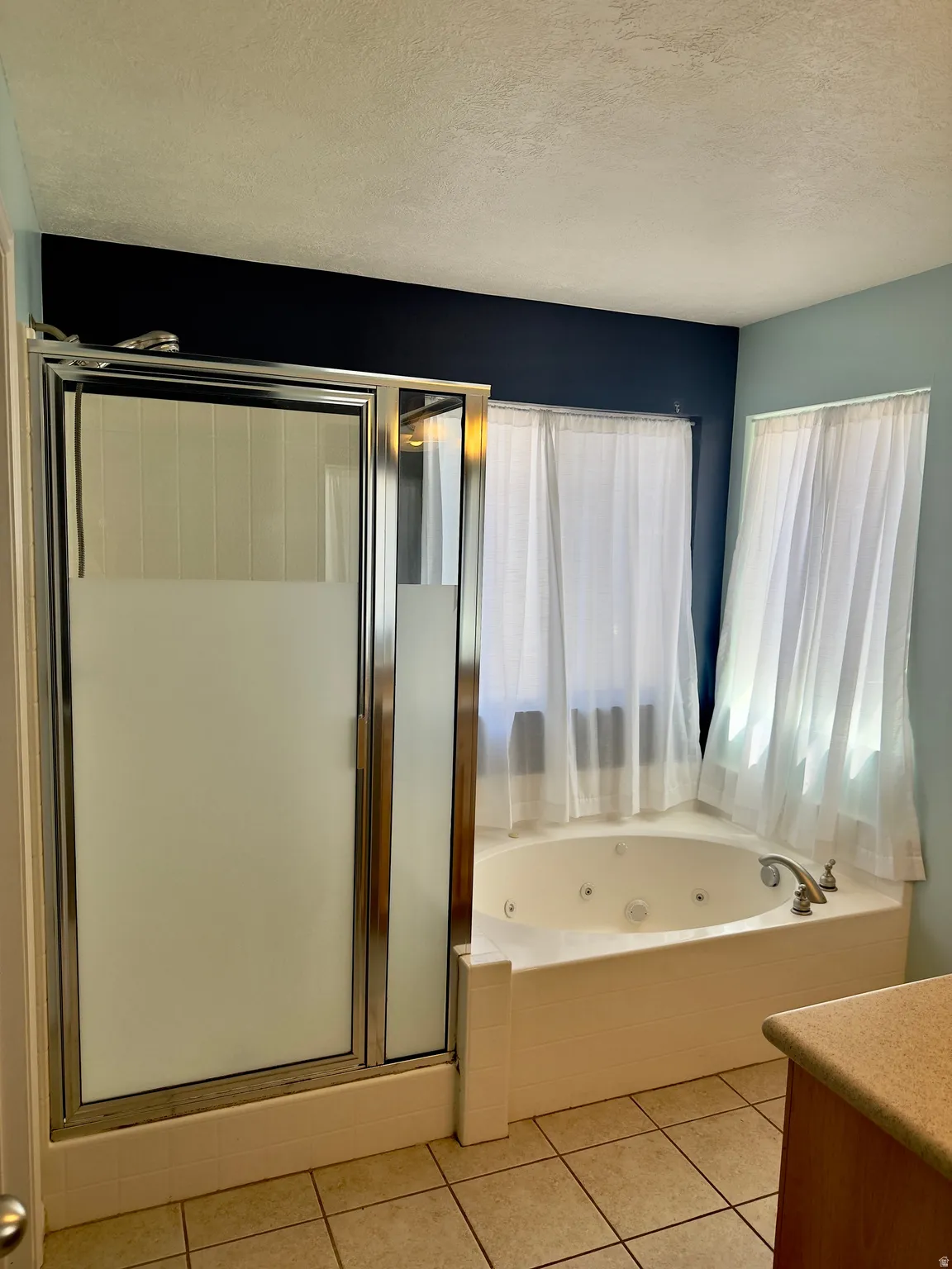 Bathroom featuring a corner jetted tub with brushed nickel fixtures, a glass-enclosed shower with a frosted panel, and tile flooring