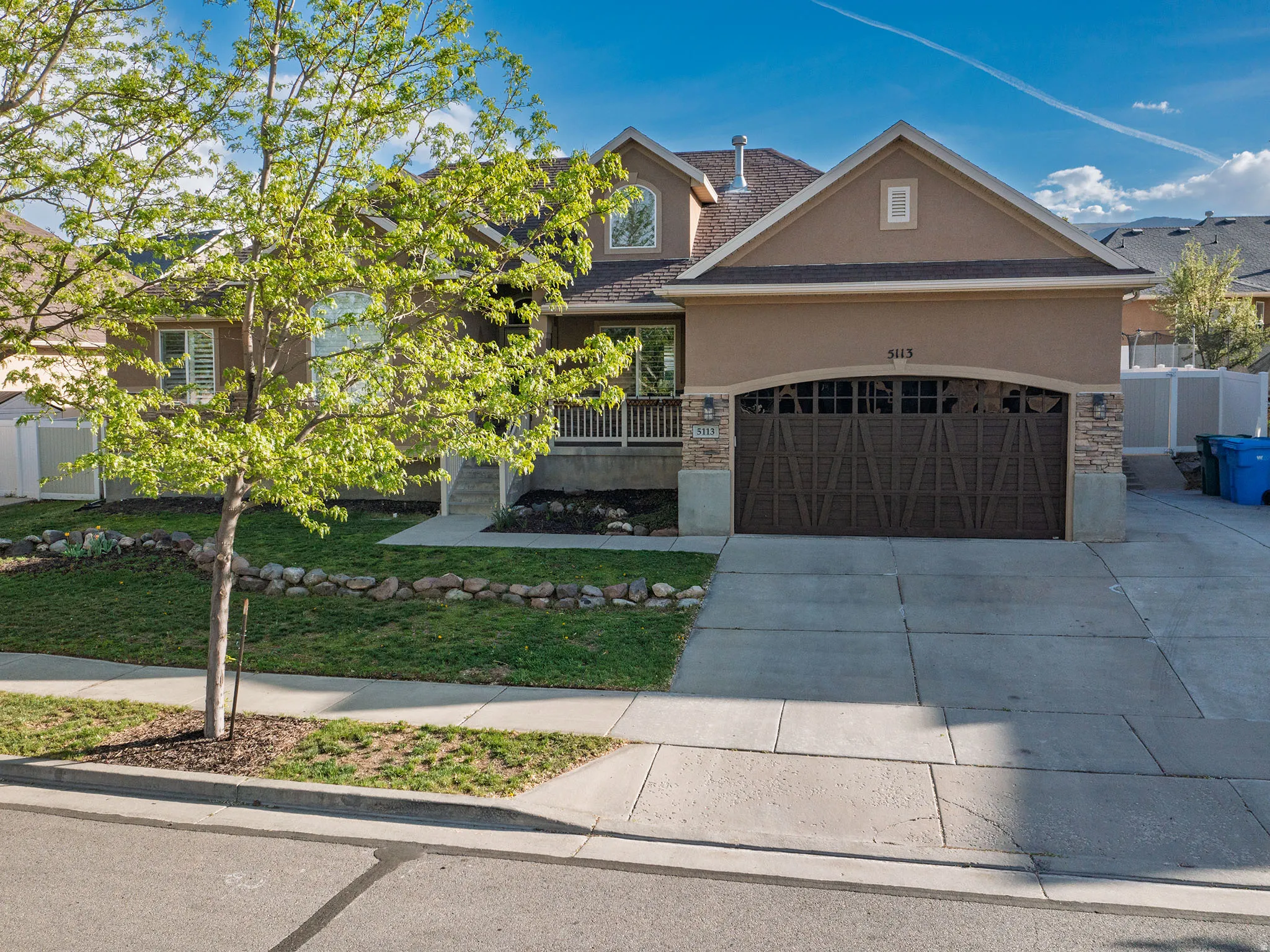 View of front facade with stucco siding, driveway, stone siding, and an attached garage