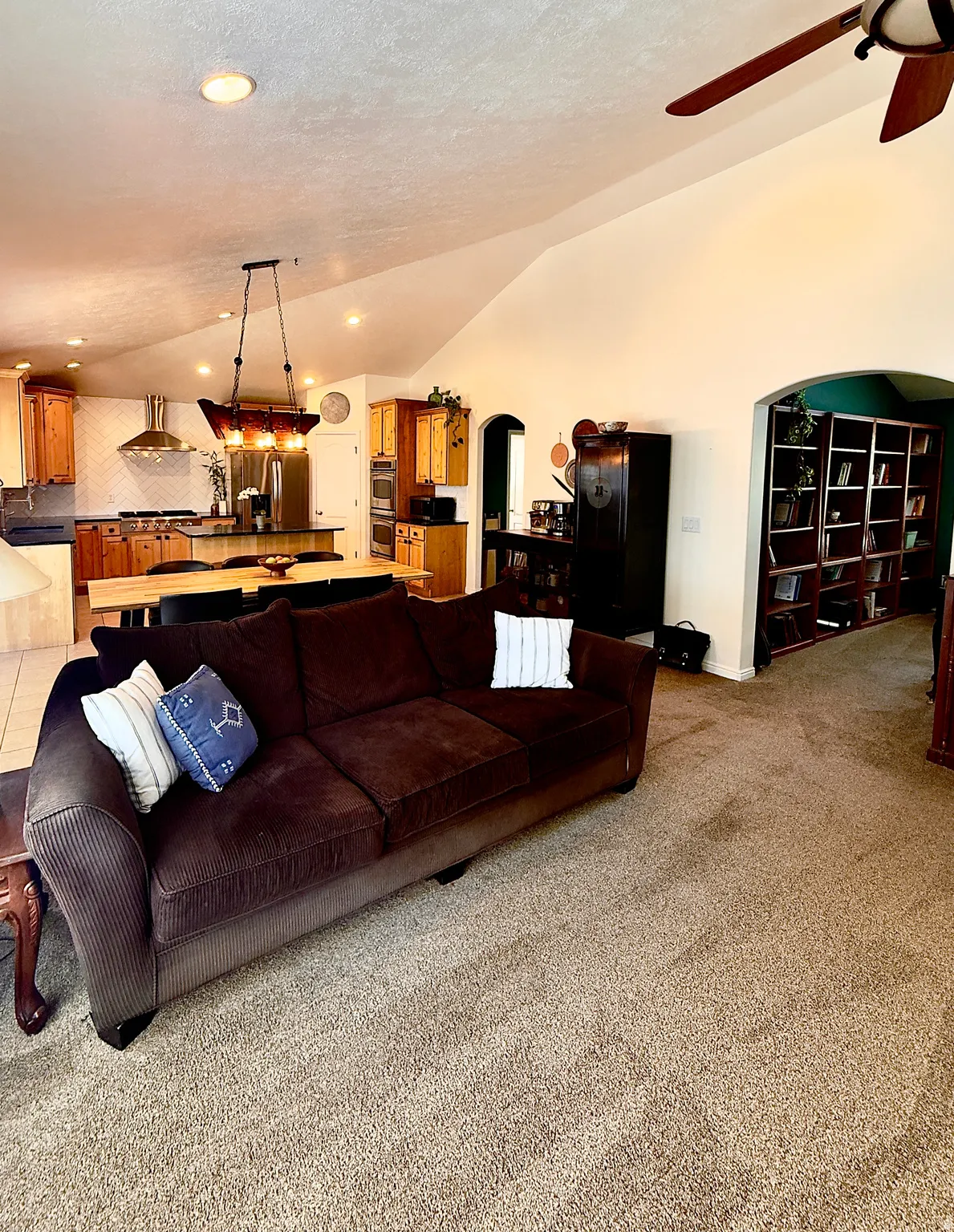 Living room featuring arched walkways, lofted ceiling, a ceiling fan, light colored carpet, and recessed lighting