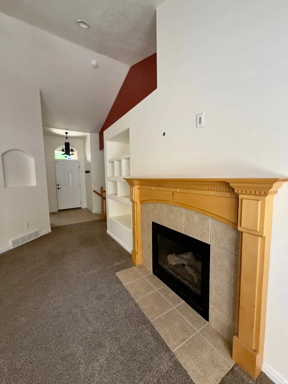 Living area featuring a gas fireplace with a tiled surround and light wood mantel, built-in shelving, high ceilings, and neutral carpeting