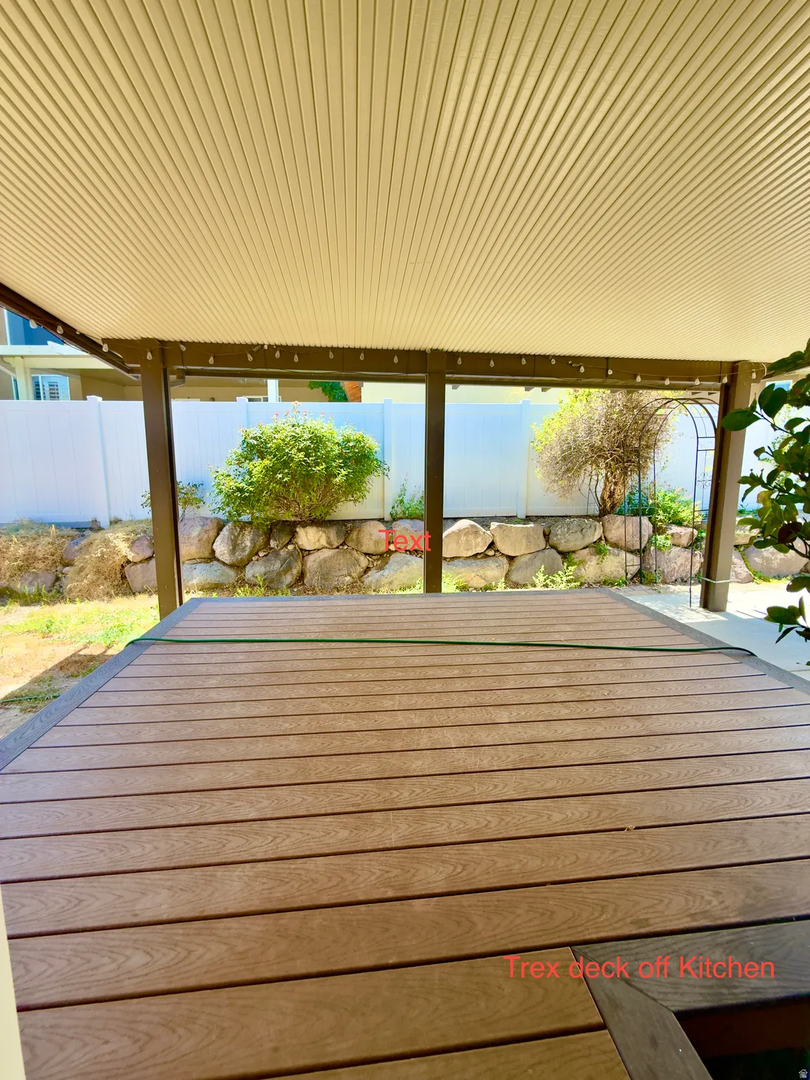 Covered patio with a composite deck, supported by brown structural beams, and featuring a white corrugated ceiling