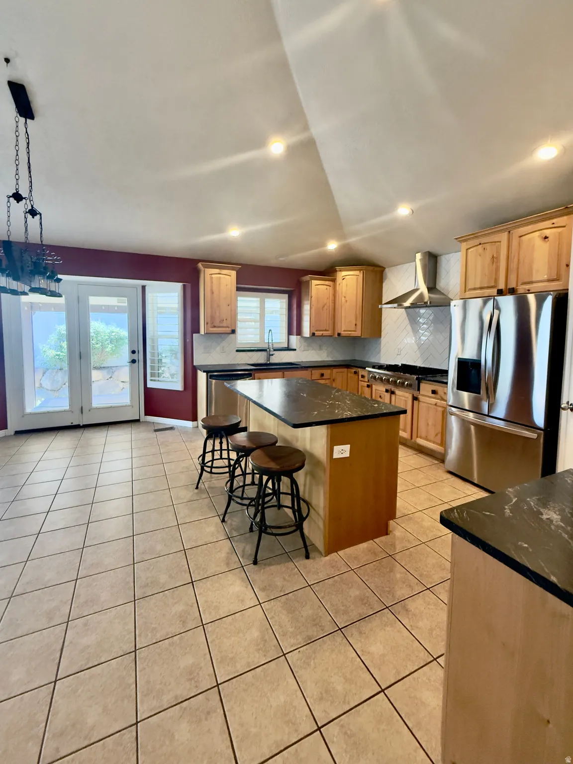 Kitchen featuring light wood cabinetry, dark stone countertops, stainless steel appliances, a center island with bar seating, and tile flooring