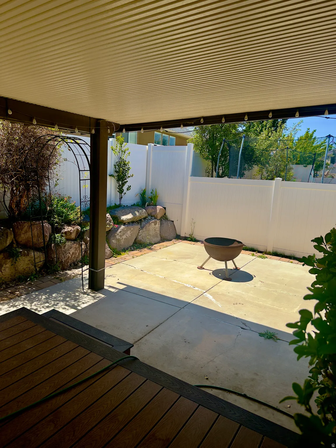 Spacious outdoor living area featuring a covered patio, composite decking, concrete patio, and rock retaining wall