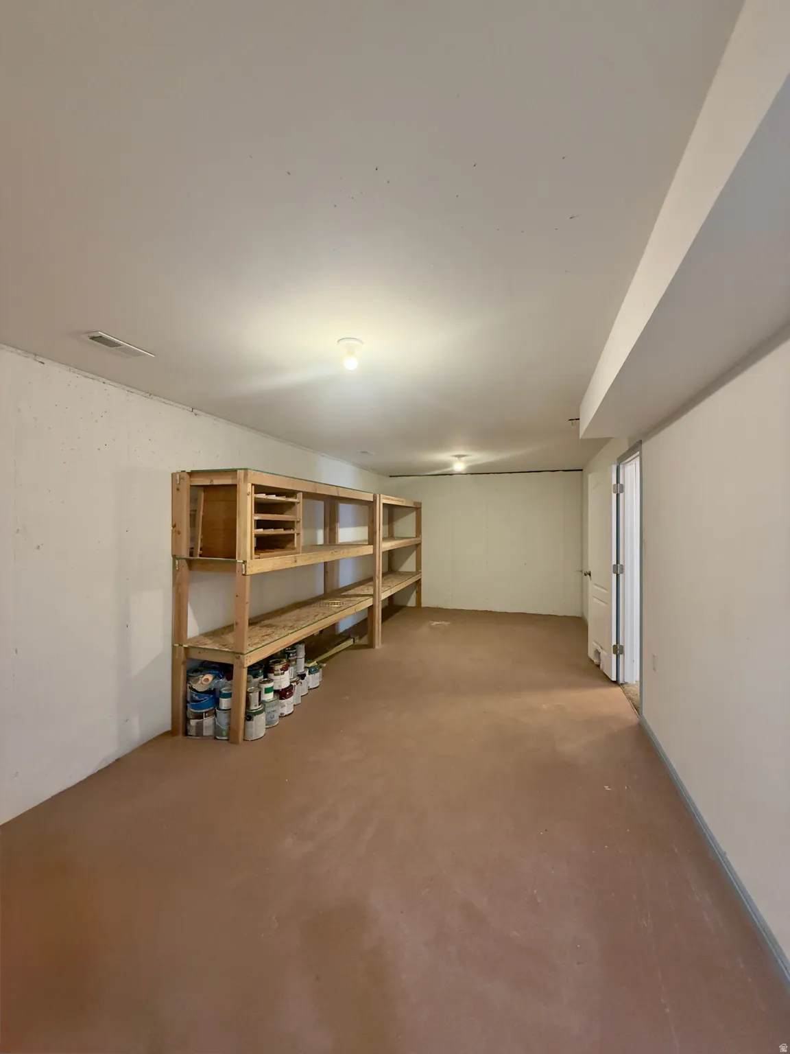 Expansive room featuring built-in wooden shelving, neutral walls, and a light brown floor