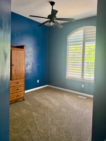 Arched window with plantation shutters, ceiling fan, and wall-to-wall carpeting