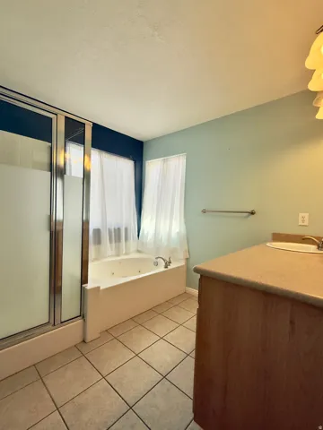 Bathroom featuring a corner jetted tub, separate shower with frosted glass doors, tile flooring, and a wood-finish vanity with an integrated sink
