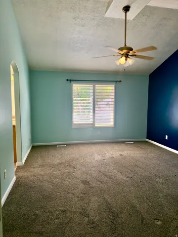 Spacious room featuring vaulted ceilings with a ceiling fan light fixture, plush carpeting, and a window with plantation shutters