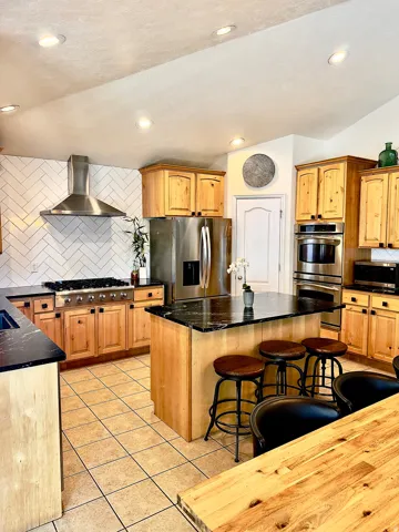 Kitchen with backsplash, stainless steel appliances, a kitchen island, light tile patterned flooring, and a breakfast bar area