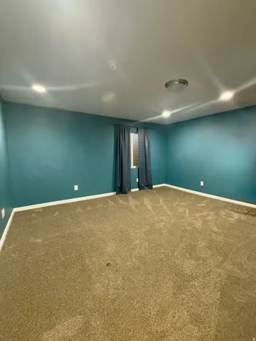 Spacious room featuring teal-painted walls, a large window with privacy blinds, and recessed lighting