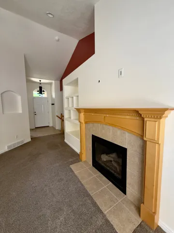Living area featuring a gas fireplace with a tiled surround and light wood mantel, built-in shelving, high ceilings, and neutral carpeting