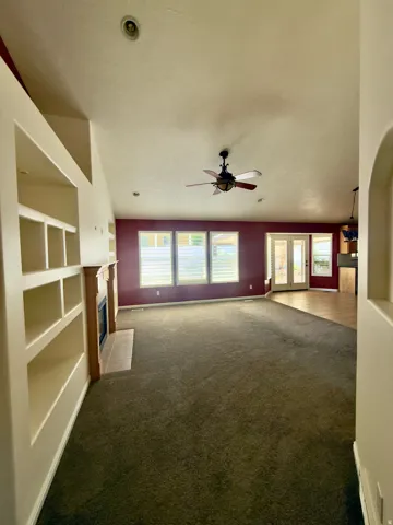 Spacious living area featuring vaulted ceilings, a ceiling fan, and built-in shelving alongside a fireplace