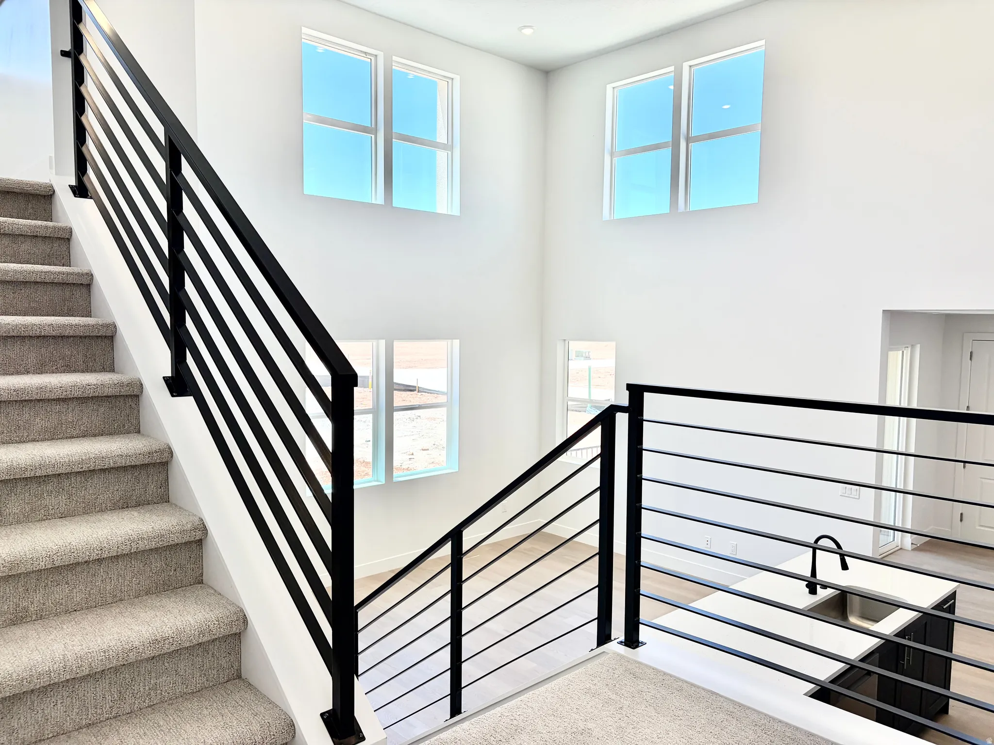 Staircase featuring dark metal horizontal railings and light-colored carpeted treads