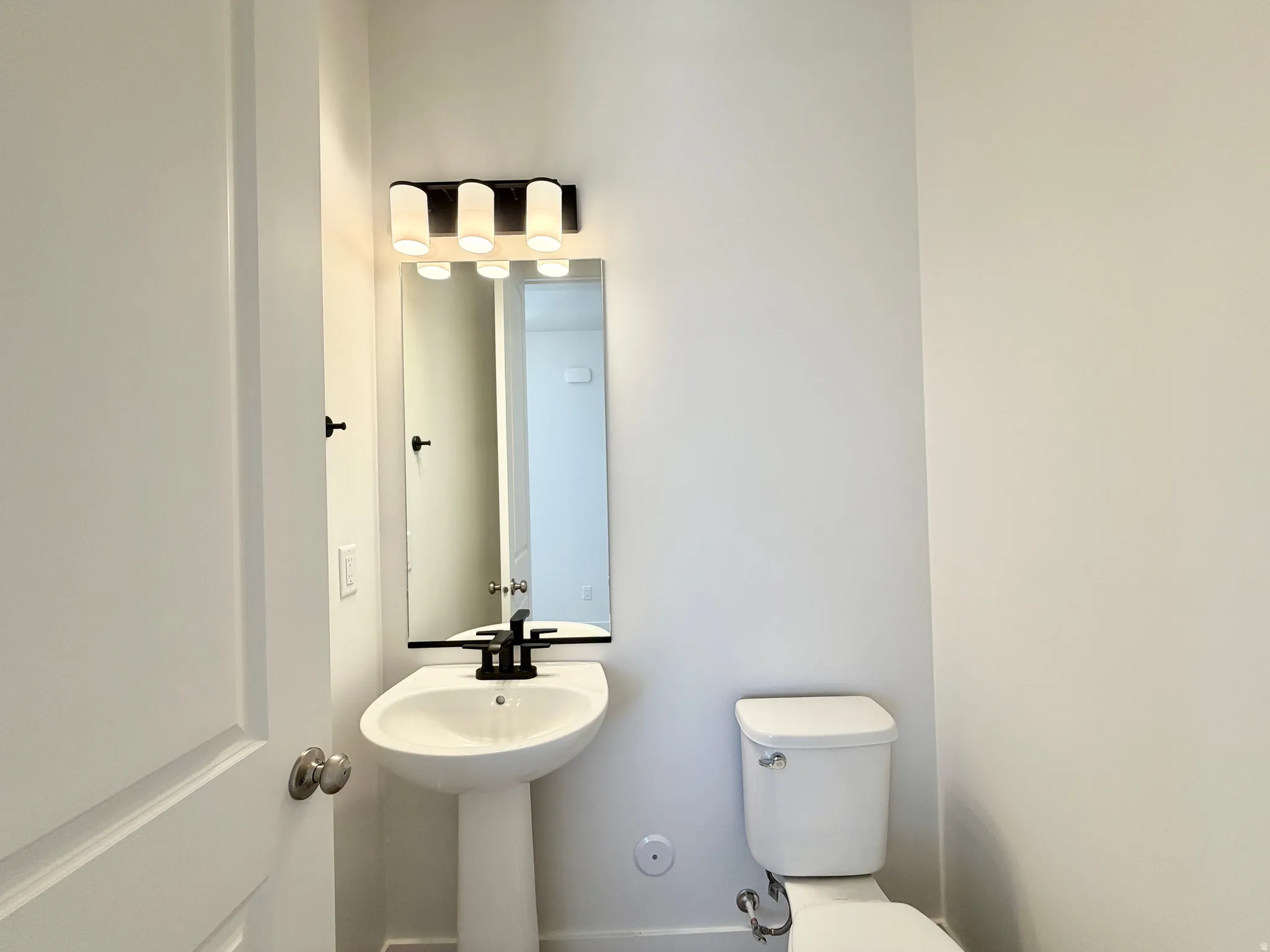 Pedestal sink with a matte black faucet, wall-mounted mirror, and a modern four-light vanity fixture
