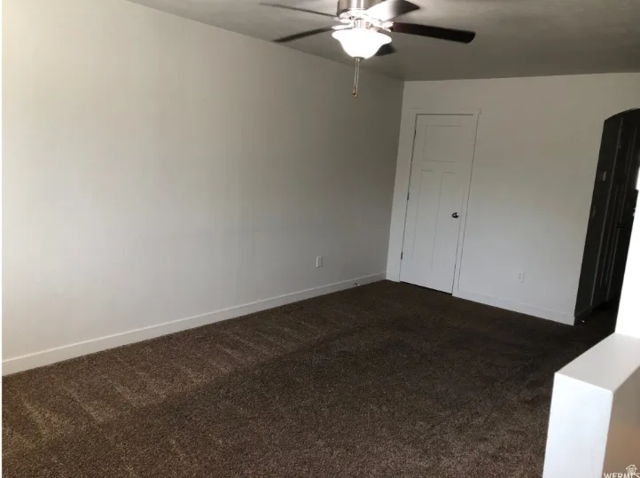 Unfurnished bedroom with dark colored carpet, arched walkways, a ceiling fan, and a closet