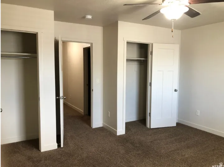 Unfurnished bedroom with two closets, dark colored carpet, and ceiling fan