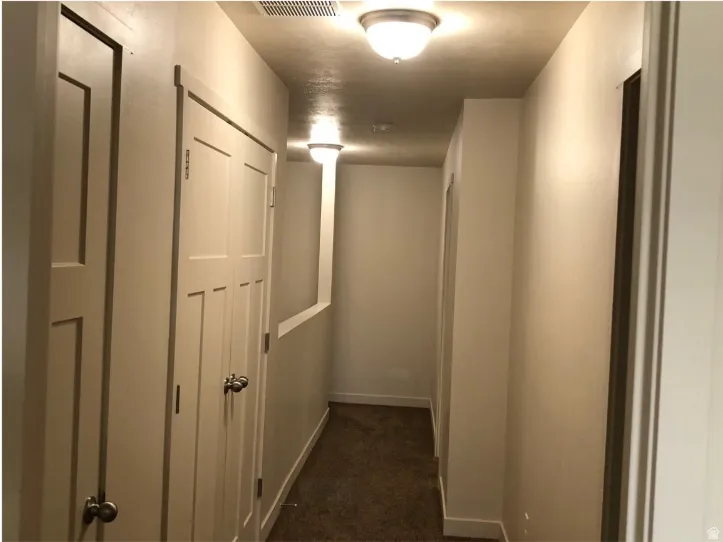 Hallway featuring baseboards and dark carpet