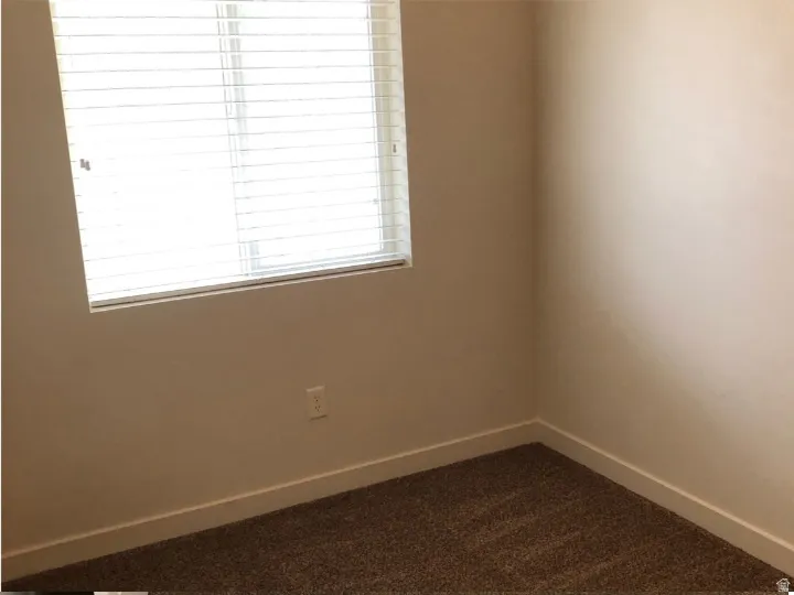 Empty room featuring baseboards and dark colored carpet