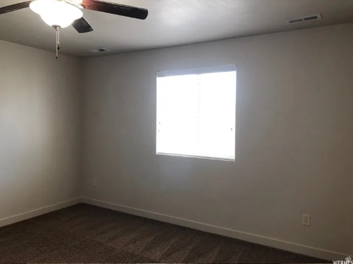 Unfurnished room featuring ceiling fan and dark colored carpet