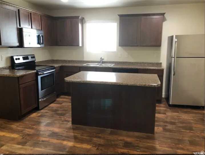 Kitchen with dark wood finish cabinetry, stainless steel appliances, a center island, and dark wood-style floors