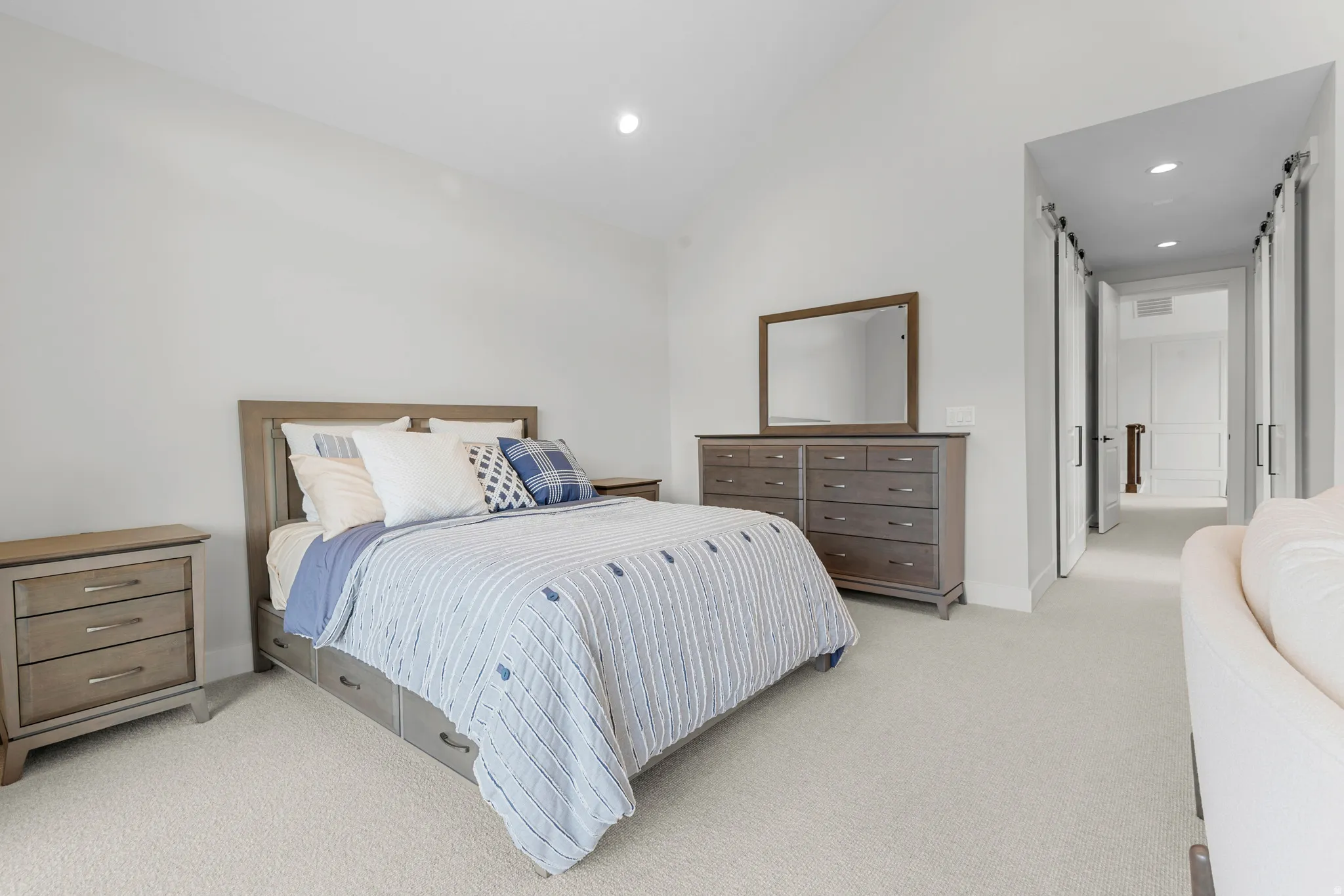 Bedroom featuring a barn door, lofted ceiling, light carpet, and recessed lighting